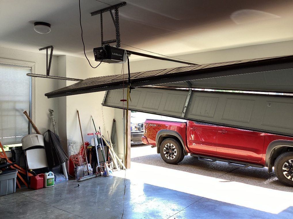 Garage door pulled off its track, hanging at an angle and blocking a truck in the bay