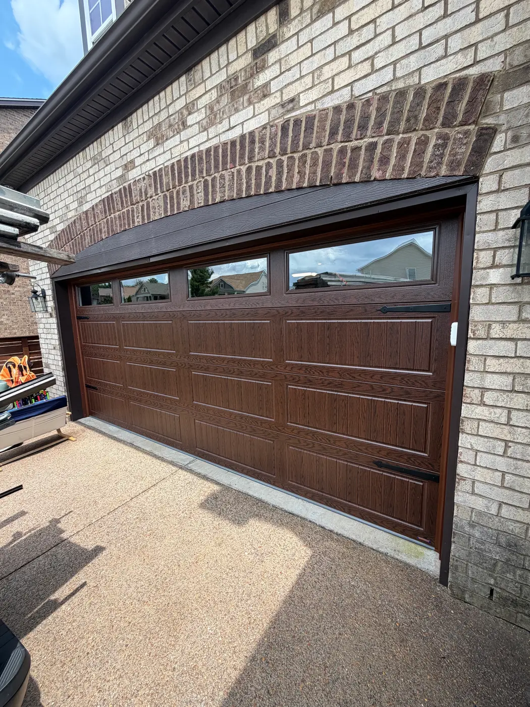 Dad & Daughter garage door project, new walnut woodgrain carriage door shown mid-open on a brick home